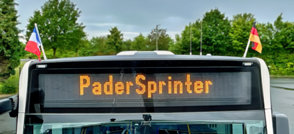 Zielanzeige eines Busses mit dem Text "PaderSprinter". Links ist die französische Flagge, rechts die deutsche Flagge am Bus angebracht.