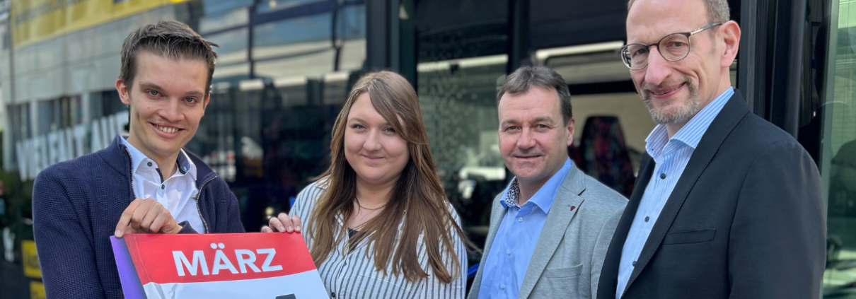 Vier Mitarbeiter des PaderSprinter stehen vor einem Bus und halten ein Plakat mit dem Motiv des Fahrplanswechsels hoch.