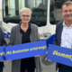 Drei Personen stehen vor einem Gelenkbus und zeigen jeweils ein Schild mit den Aufschriften "#meinlieblingsbus", "Mit Bestnoten unterwegs" sowie "#kommtgutan"