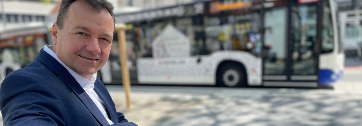 PaderSprinter-Geschäftsführer Oliver Eikenberg sitzt auf einer Bank und schaut in die Kamera, während im Hintergrund ein PaderSprinter-Bus steht