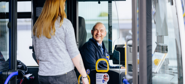 Ein Fahrgast wird vom Busfahrer in einem Bus herzlich begrüßt