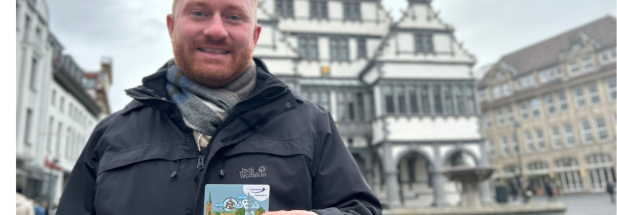 Mitarbeiter des PaderSprinter präsentiert die neue Chipkarte vor dem historischen Rathaus von Paderborn