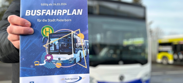 Ein Mitarbeiter zeigt das Fahrplanheft ab 24.03.2024 vor einem PaderSprinter-Bus