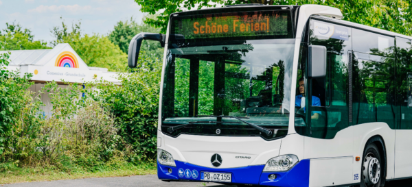 Ein Bus steht vor einer Grundschule mit dem Zieltext "Schöne Ferien!"